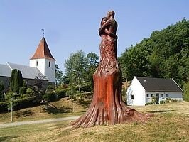 Gravlev Kirke i baggrunden og i forgrunden træskulpturen Størst af alt er kærligheden