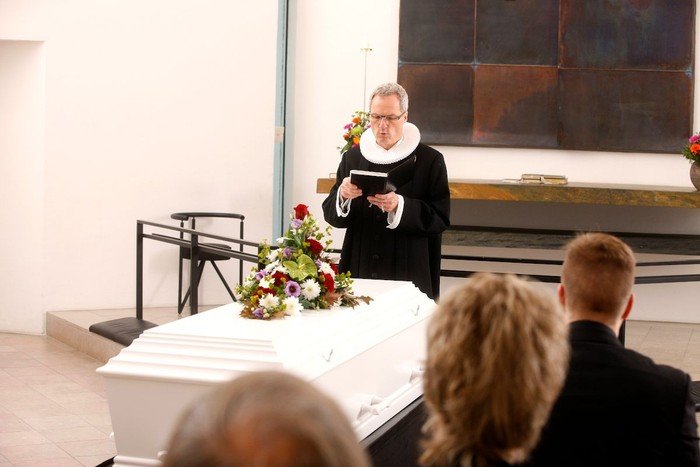 En præst står ved i pyntet kiste i en kirke