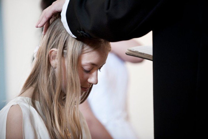 Konfirmand konfirmeres. Præst har lagt hånden på konfirmandens hoved